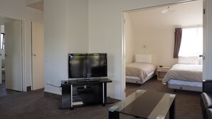 A hotel room with a flat-screen TV on a stand, a glass coffee table, a bed, a bedside table, and a window with curtains. - Ashleigh Court Motel-Christchurch Hagley Park (Christchurch)