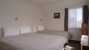 Una habitación de hotel con dos camas, una ventana pequeña con cortinas, un cuadro en la pared y una mesita de noche de madera.