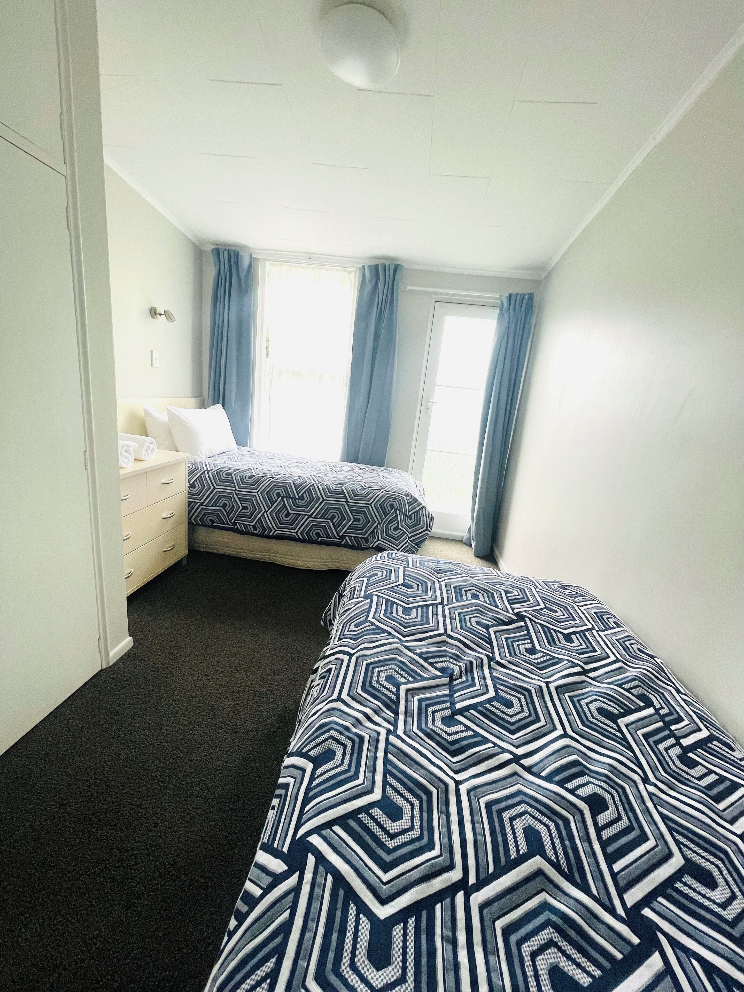 Ein Zimmer mit zwei Betten, einem Schminktisch, einem Fenster mit Vorhängen und einer Deckenleuchte.