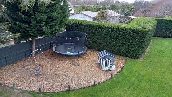 A backyard with a trampoline, a swing set, and a small playhouse. - Northwood Motor Lodge (Christchurch)
