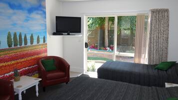 Una stanza con una televisione montata a parete, una poltrona rossa, un divano grigio con cuscini verdi e vista su un giardino tramite una porta scorrevole in vetro.