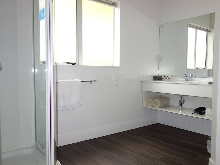A bathroom with a glass shower door, a white towel hanging on a towel bar, a white sink with a mirror above it, and a shelf with toiletries.