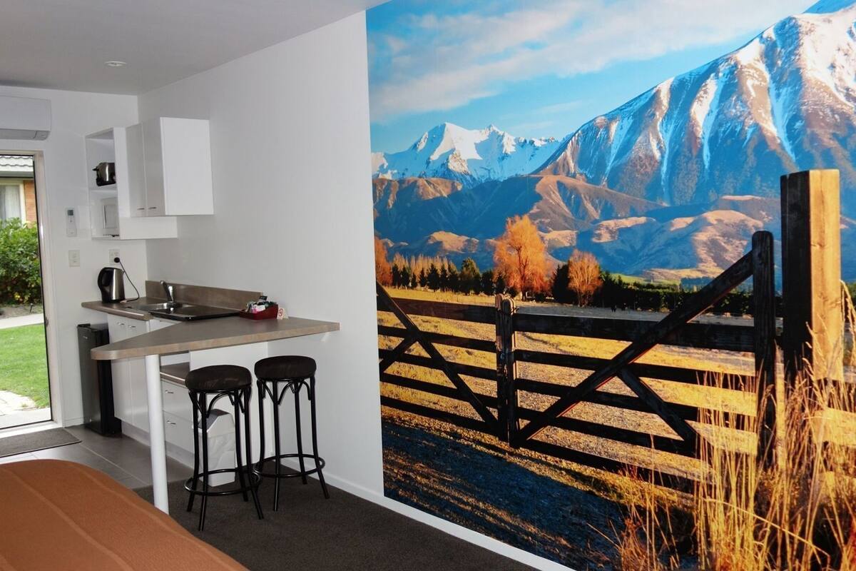 A modern kitchen with a dining area, a large window, and a mural of a mountain landscape.