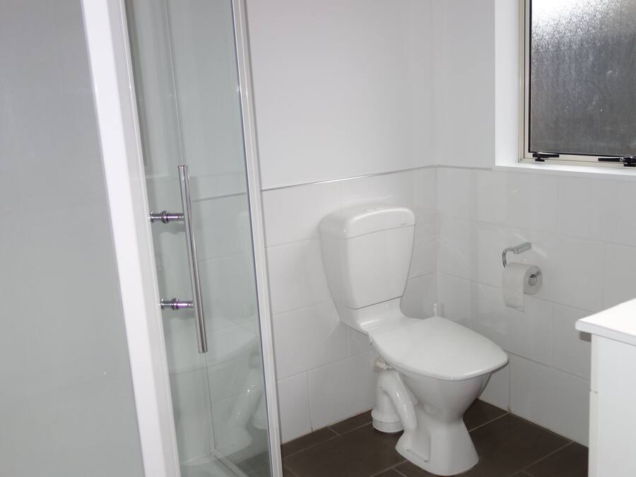 Casa de banho com sanita, cabine de duche em vidro e rolo de papel higiénico.