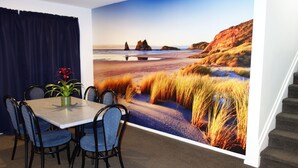 Een eethoek met een tafel en stoelen, een kamerplant en een grote strandmuur aan de wand.