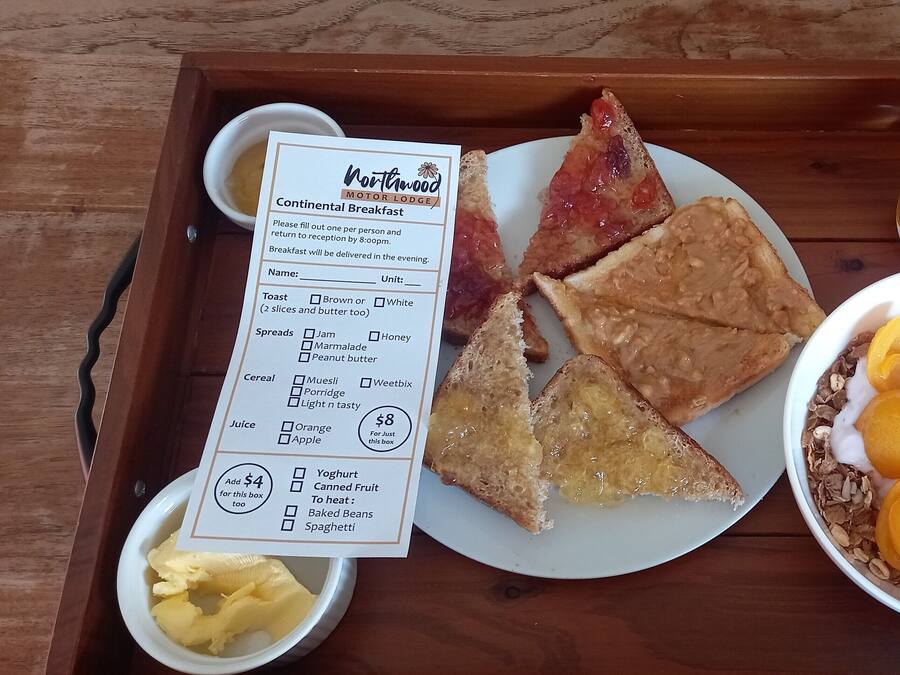 A breakfast tray with toast, a bowl of cereal with fruit, a glass of orange juice, and a menu from Northwood Motor Lodge.