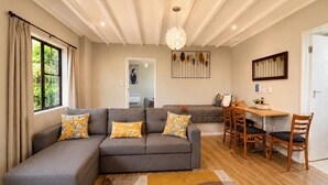 A modern living room with a sectional sofa, a dining area with wooden chairs, a rug, and a pendant light. - Gothic Heights Motel (Christchurch)
