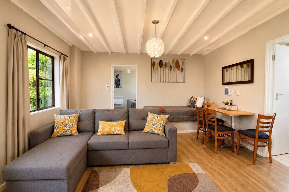 A modern living room with a sectional sofa, a dining area with wooden chairs, a rug, and a pendant light.