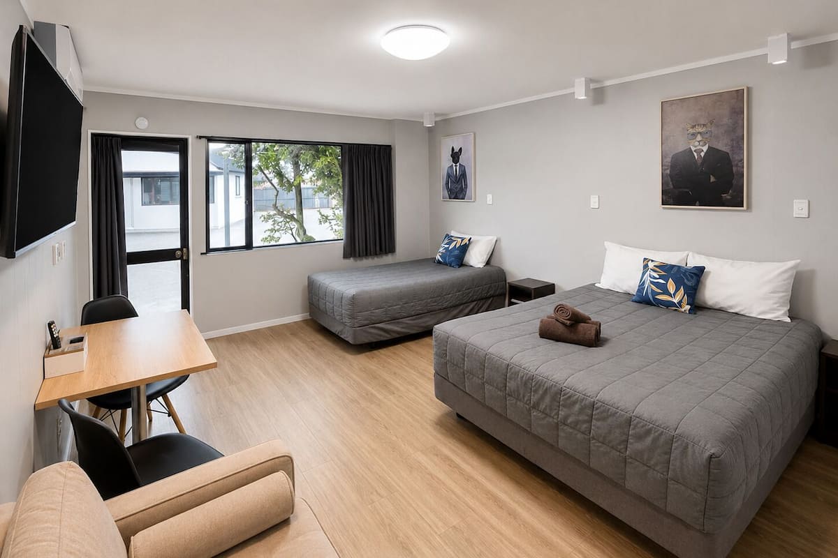 A hotel room with two beds, a desk, a chair, and a TV.