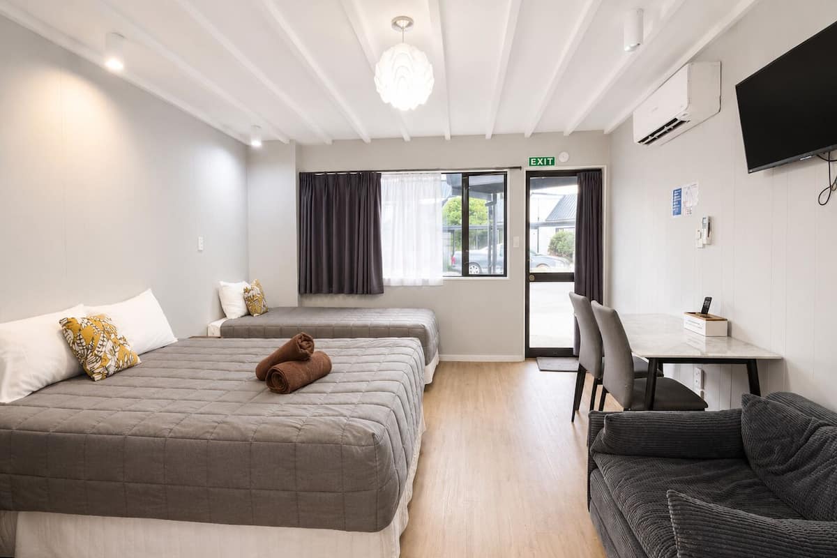 A hotel room with two beds, a desk, a chair, and a TV.