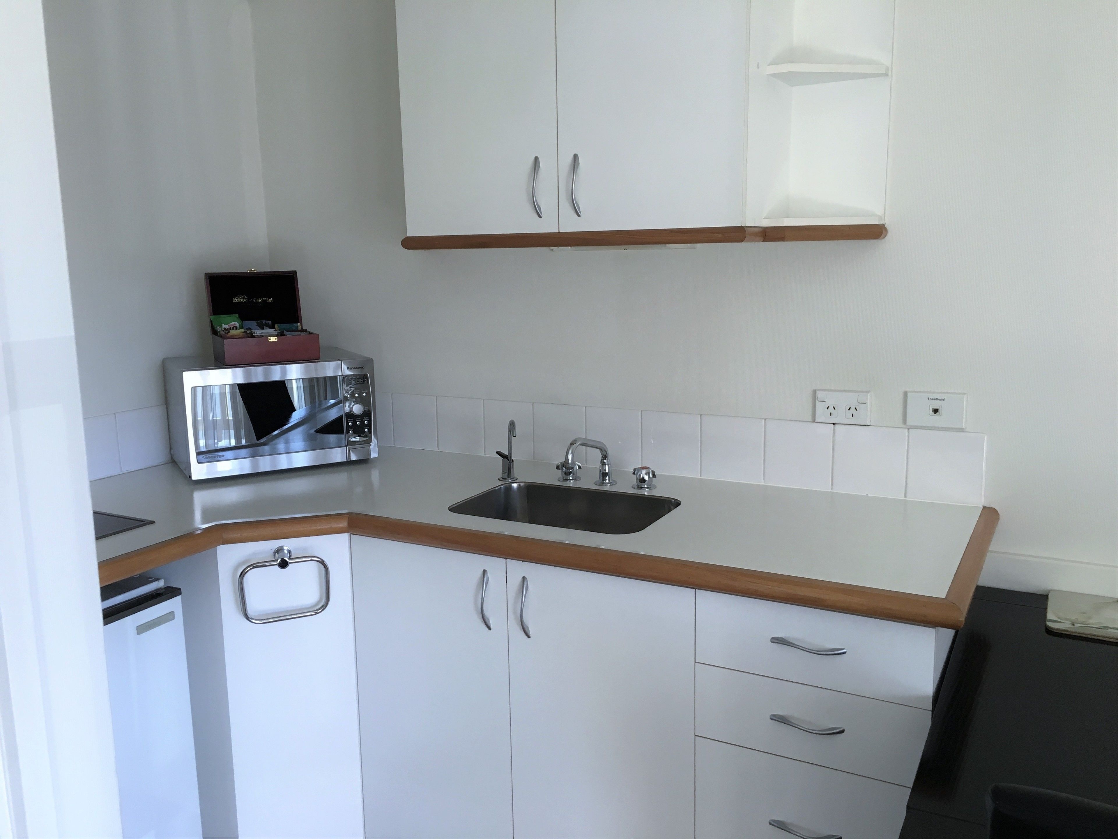 A compact kitchen with white cabinets, a stainless steel microwave, a sink, and a wooden countertop.