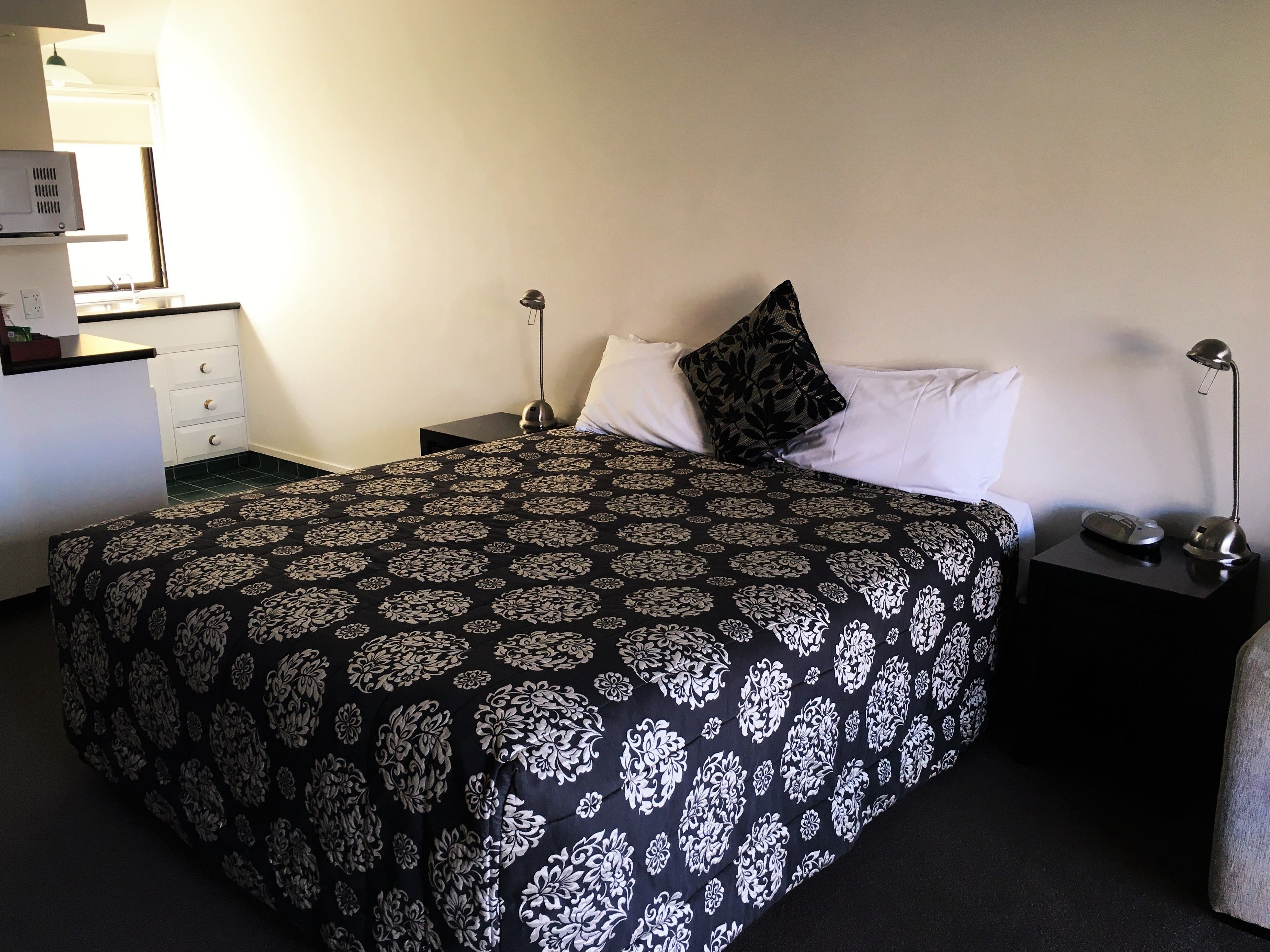 A neatly made bed with a patterned bedspread, a bedside lamp, and a small bedside table with a lamp and a phone.