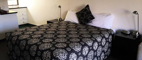 A neatly made bed with a patterned bedspread, a bedside lamp, and a small bedside table with a lamp and a phone.
