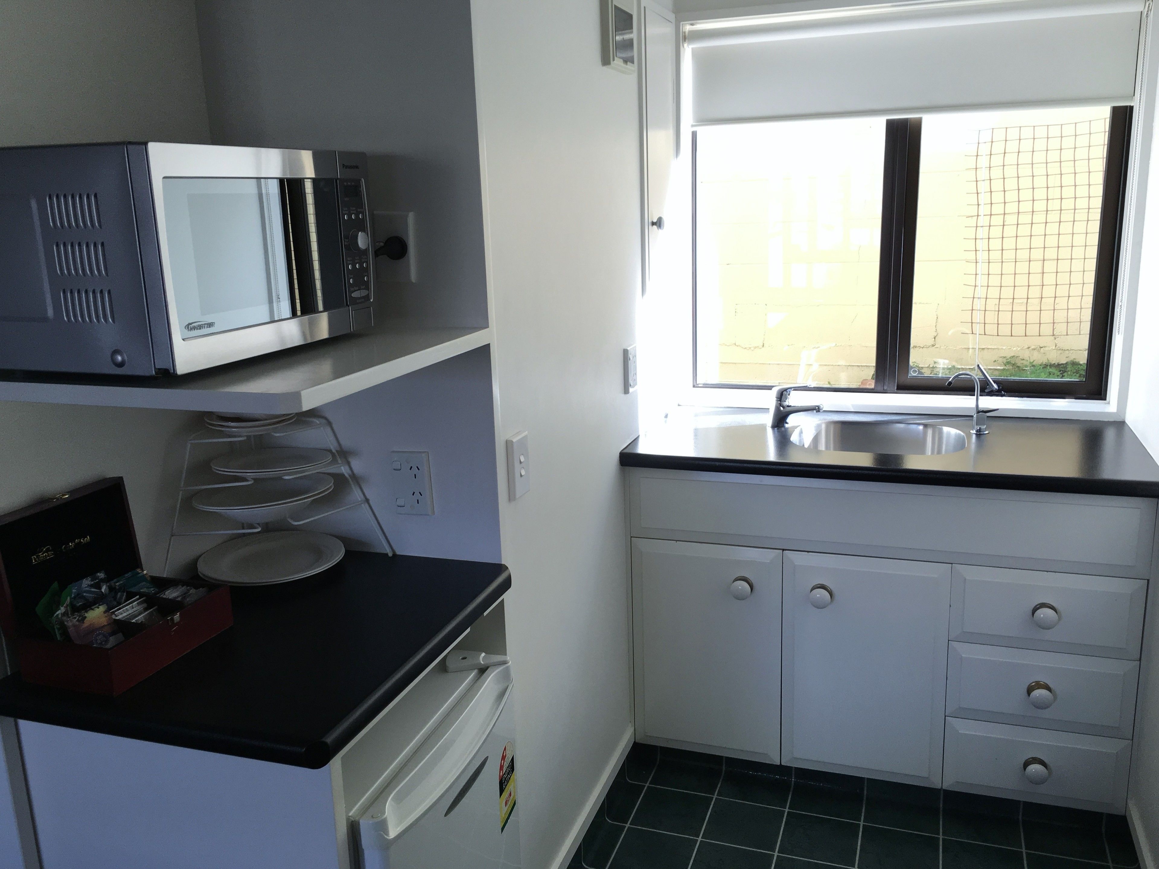 A compact kitchen with a microwave, a sink, and a window.