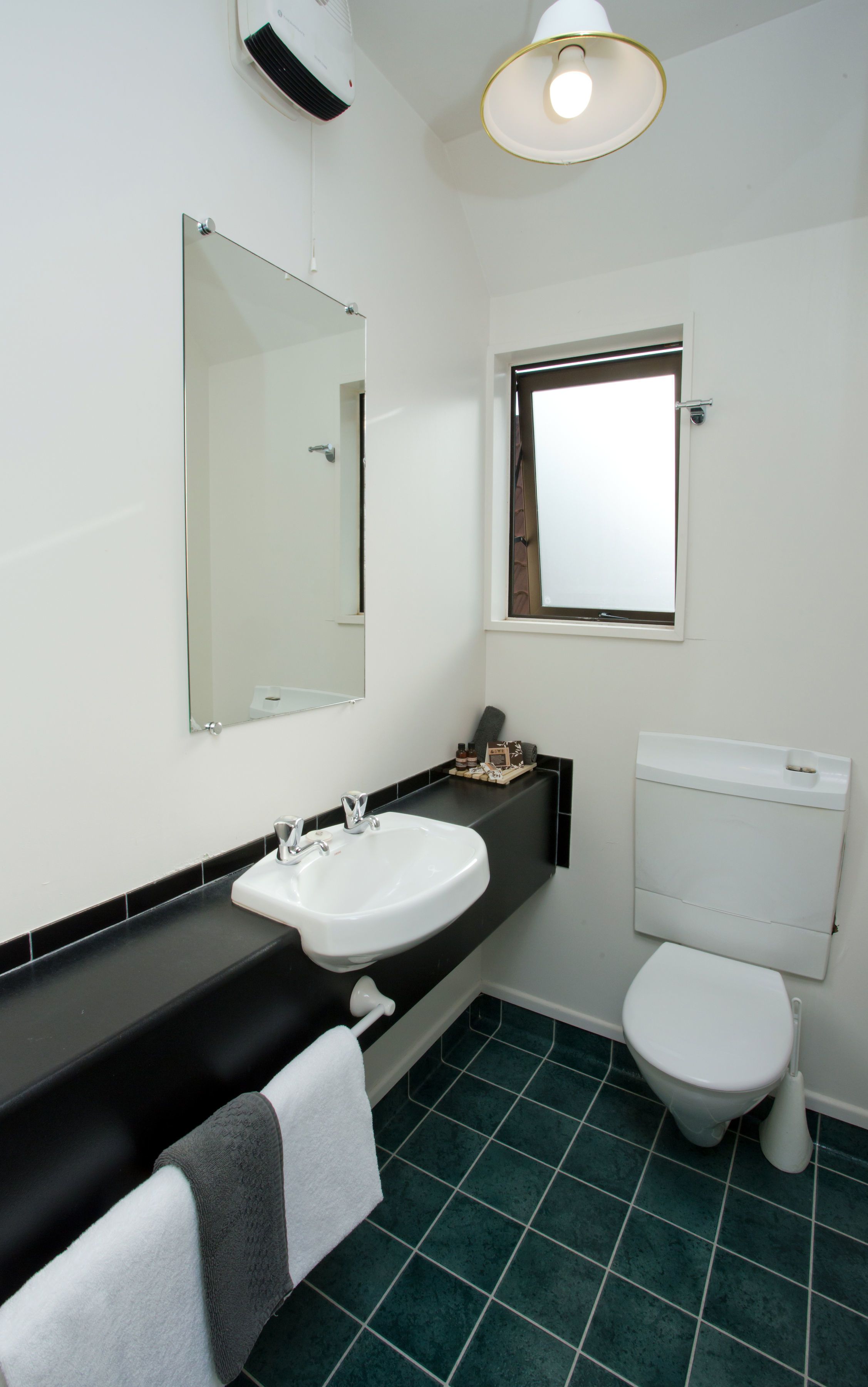 A bathroom with a white sink, a mirror, a toilet, and a window.