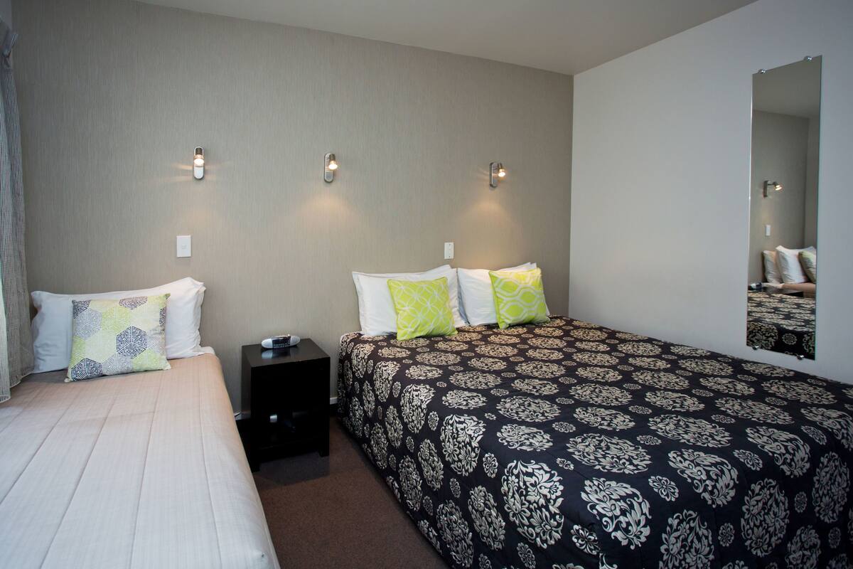 Ein Hotelzimmer mit zwei Betten, einem Nachttisch und einem großen Spiegel.