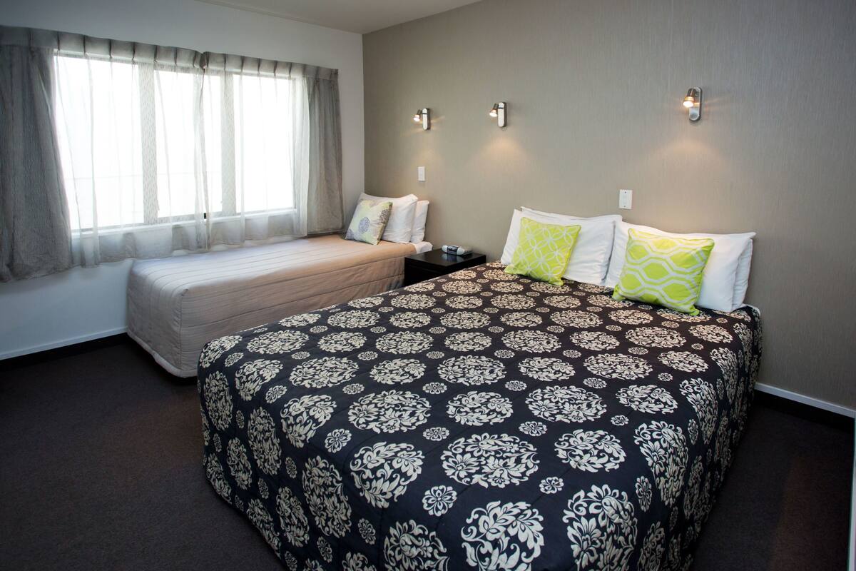Ein Hotelzimmer mit zwei Betten, einem großen Fenster mit Vorhängen und Wandleuchten.
