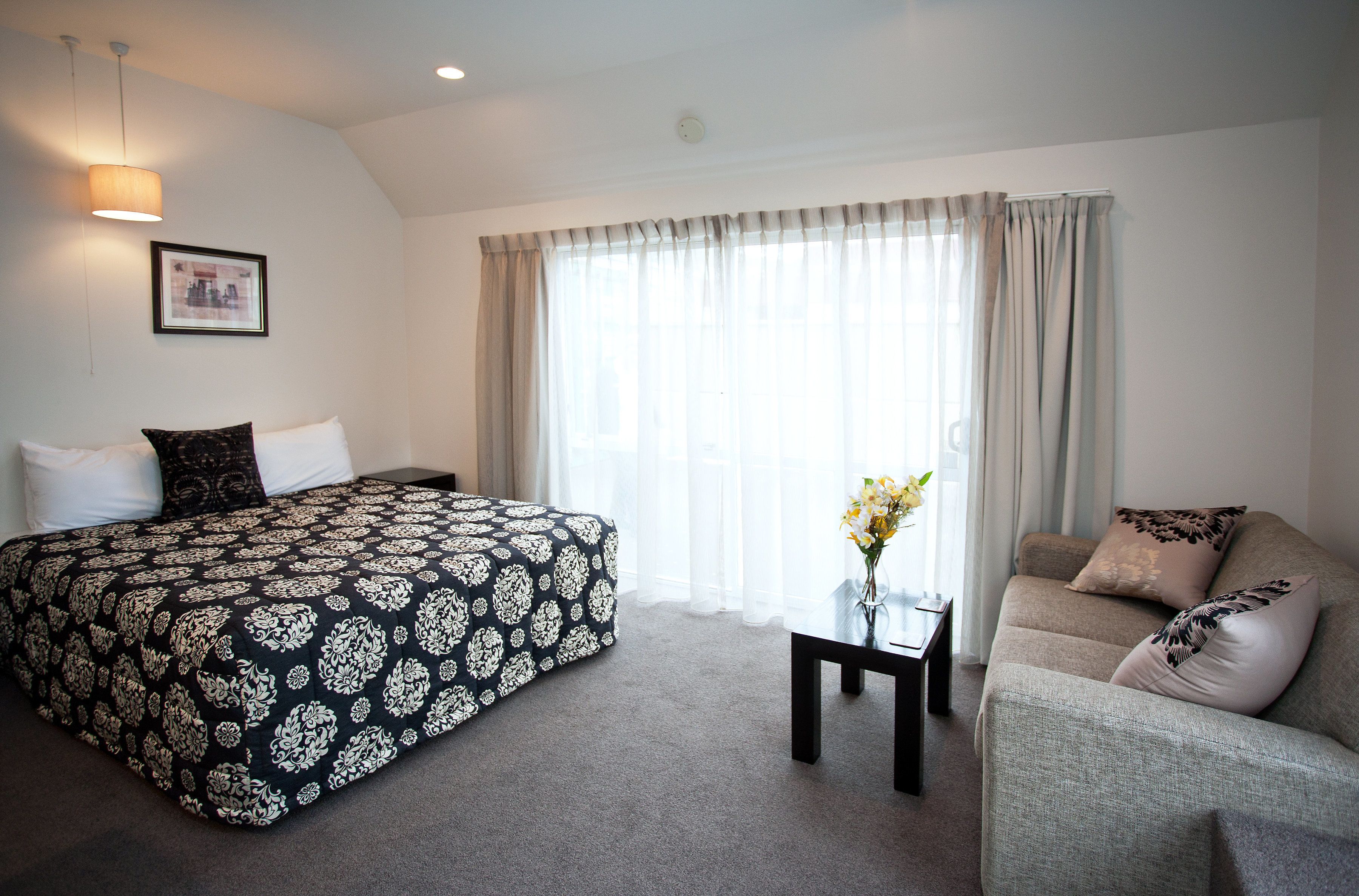 Quarto de hotel com cama, sofá, uma mesinha e janela com cortinas.