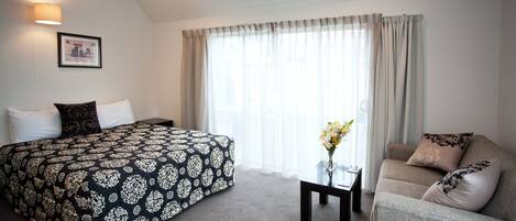 Quarto de hotel com cama, sofá, uma mesinha e janela com cortinas.