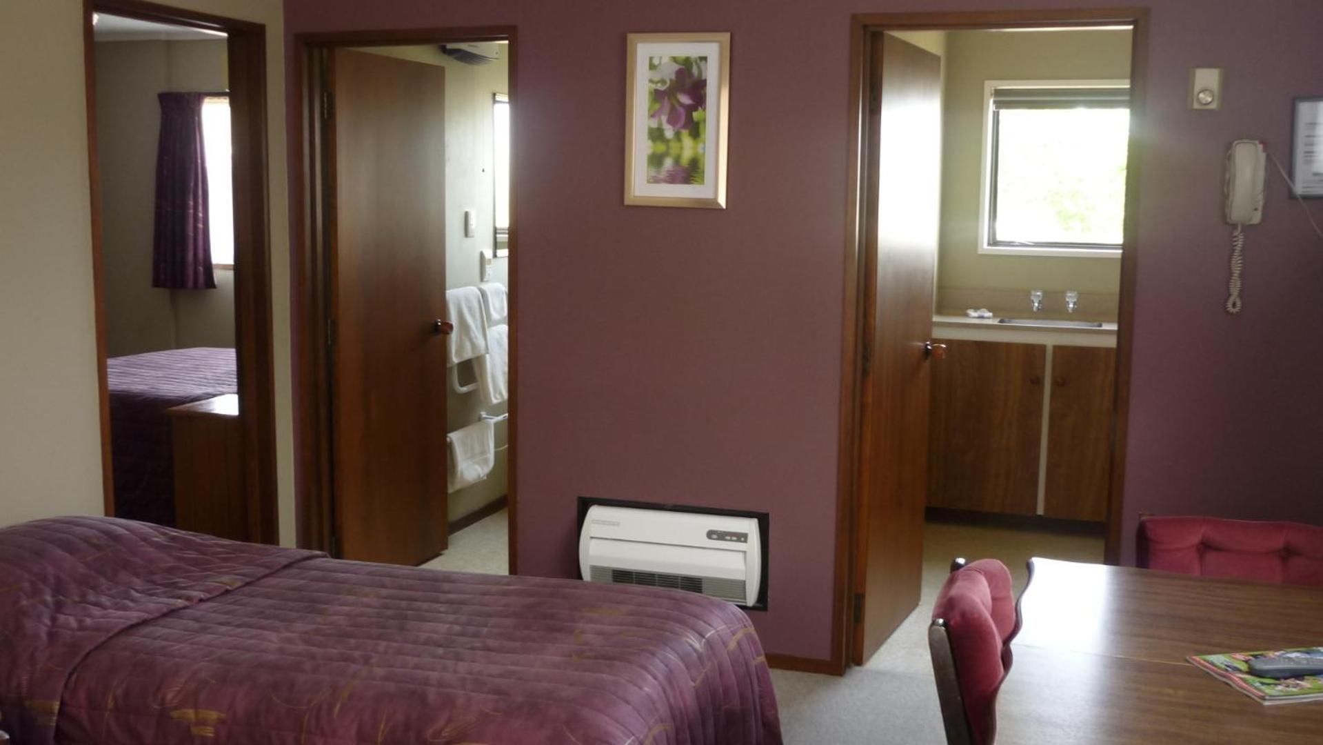 Quarto com cama, mesa, cadeira, banheiro com pia e telefone.
