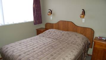 Un dormitorio con cabecera de madera, una cama con colcha estampada, dos mesitas de noche y dos lámparas de pared.