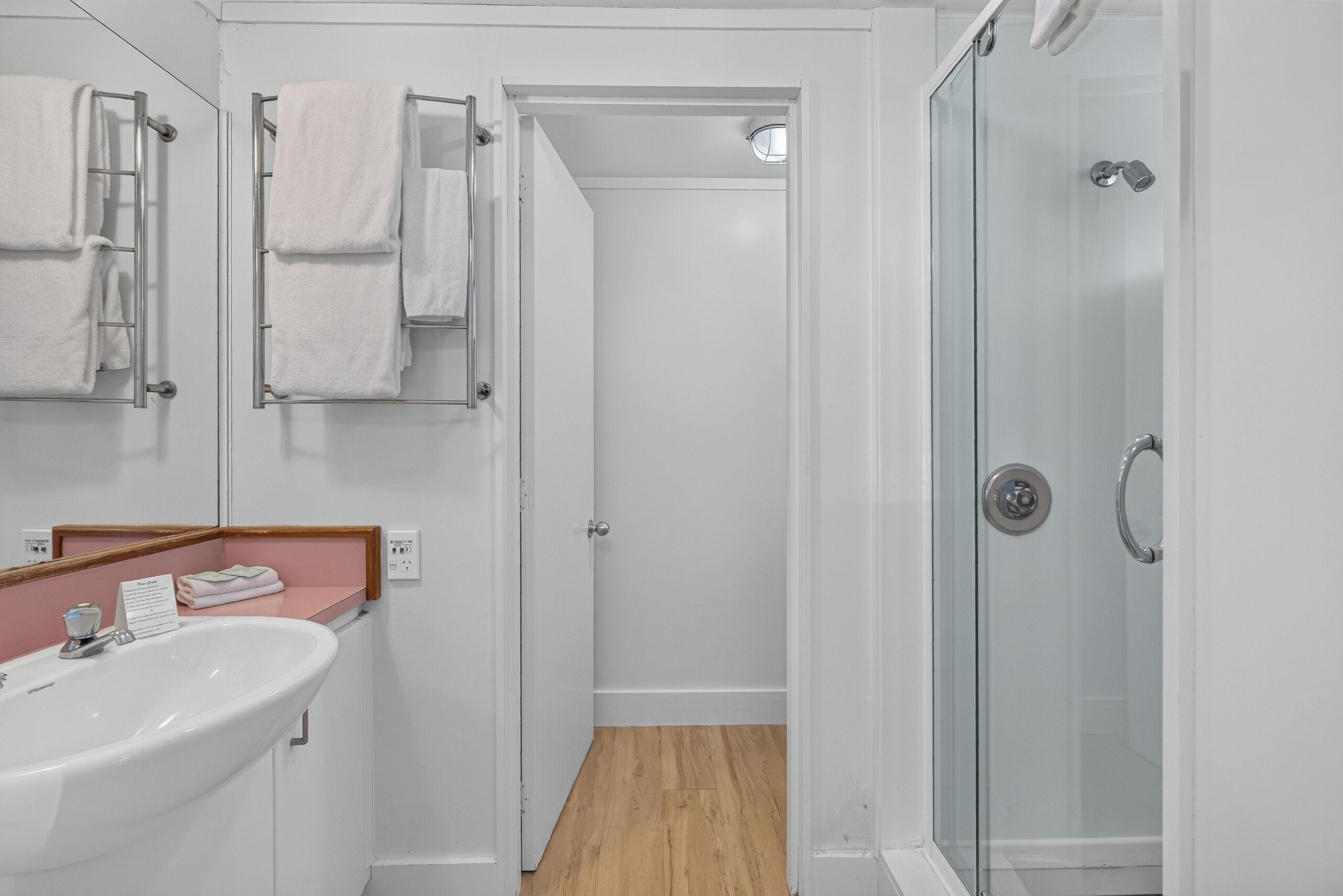 Baño con cabina de ducha de vidrio, un lavamanos blanco y un espejo encima.