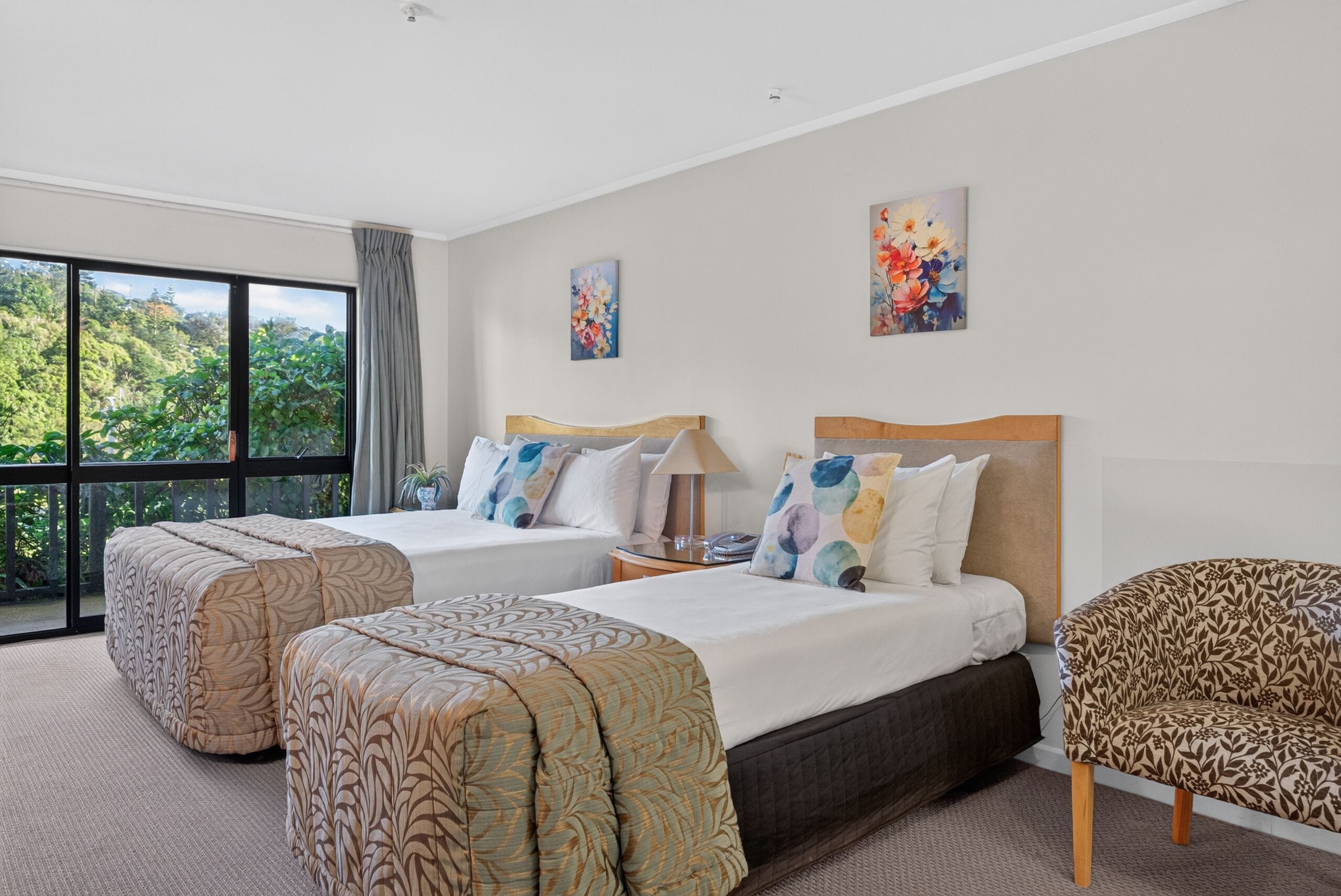 Habitación de hotel con dos camas, un ventanal grande y vistas al verdor.