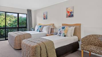 Habitación de hotel con dos camas, un ventanal grande y vistas al verdor.