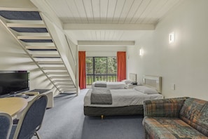 A hotel room with a staircase, two beds, a desk with a TV, and a sofa.