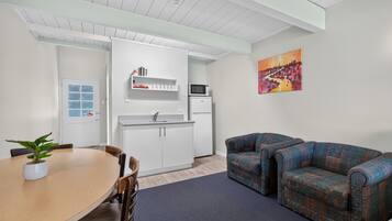 A compact living space with a dining table, two armchairs, a kitchenette, and a painting on the wall.