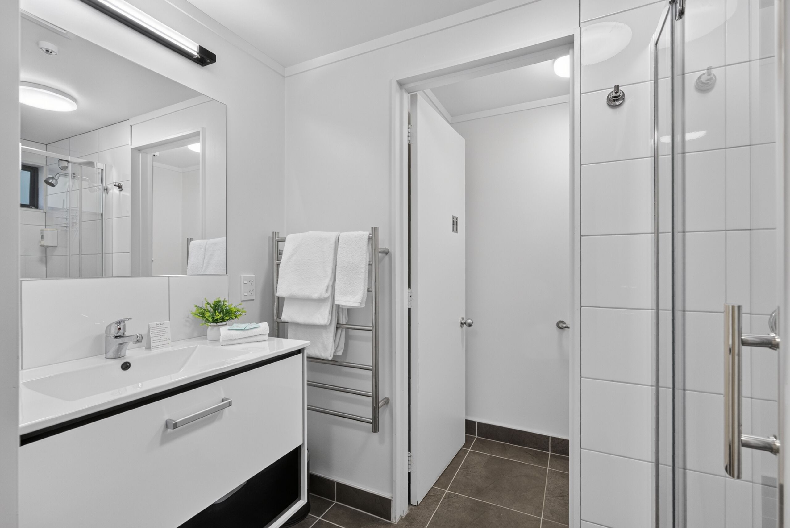 Um banheiro moderno com toucador branco, espelho, chuveiro e porta-toalhas.