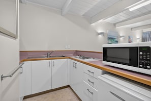 Una cocina moderna con armarios blancos, encimera de madera, microondas empotrado y pileta de acero inoxidable.