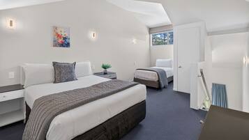 A modern bedroom with a large bed, a smaller bed, a nightstand with a plant, and a painting on the wall.