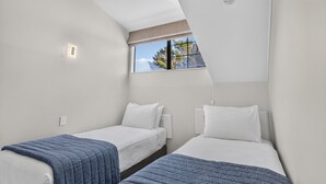 A twin room with two single beds, a window with a view of trees, and a small wall-mounted light. - Capital Lodge Motor Inn (Wellington)