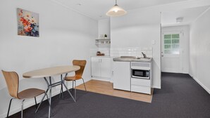 A compact kitchen with a dining table and chairs, a microwave, and a hanging light fixture. - Capital Lodge Motor Inn (Wellington)