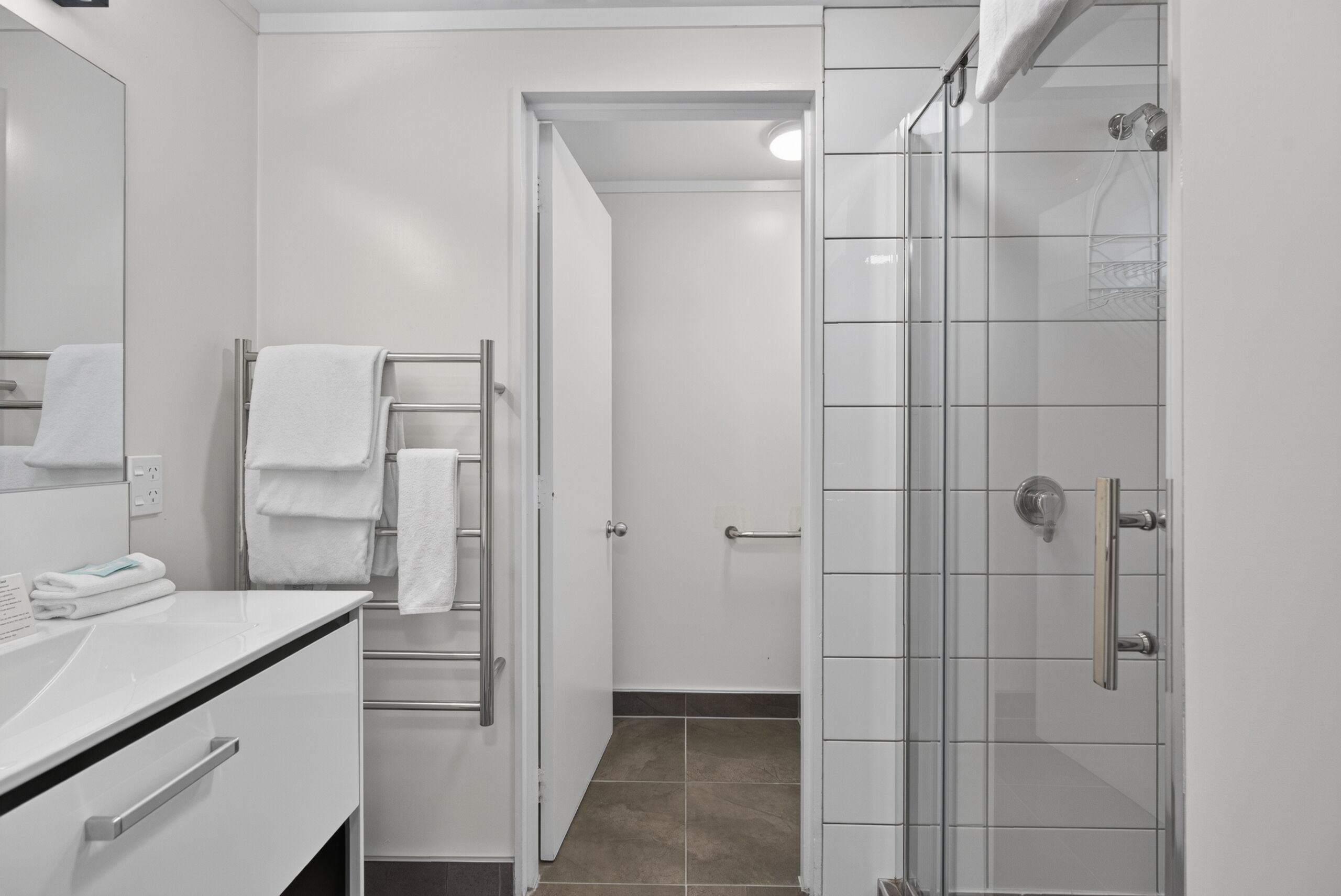 A modern bathroom with a glass shower enclosure, a white sink with a mirror, and a towel rack with folded towels.