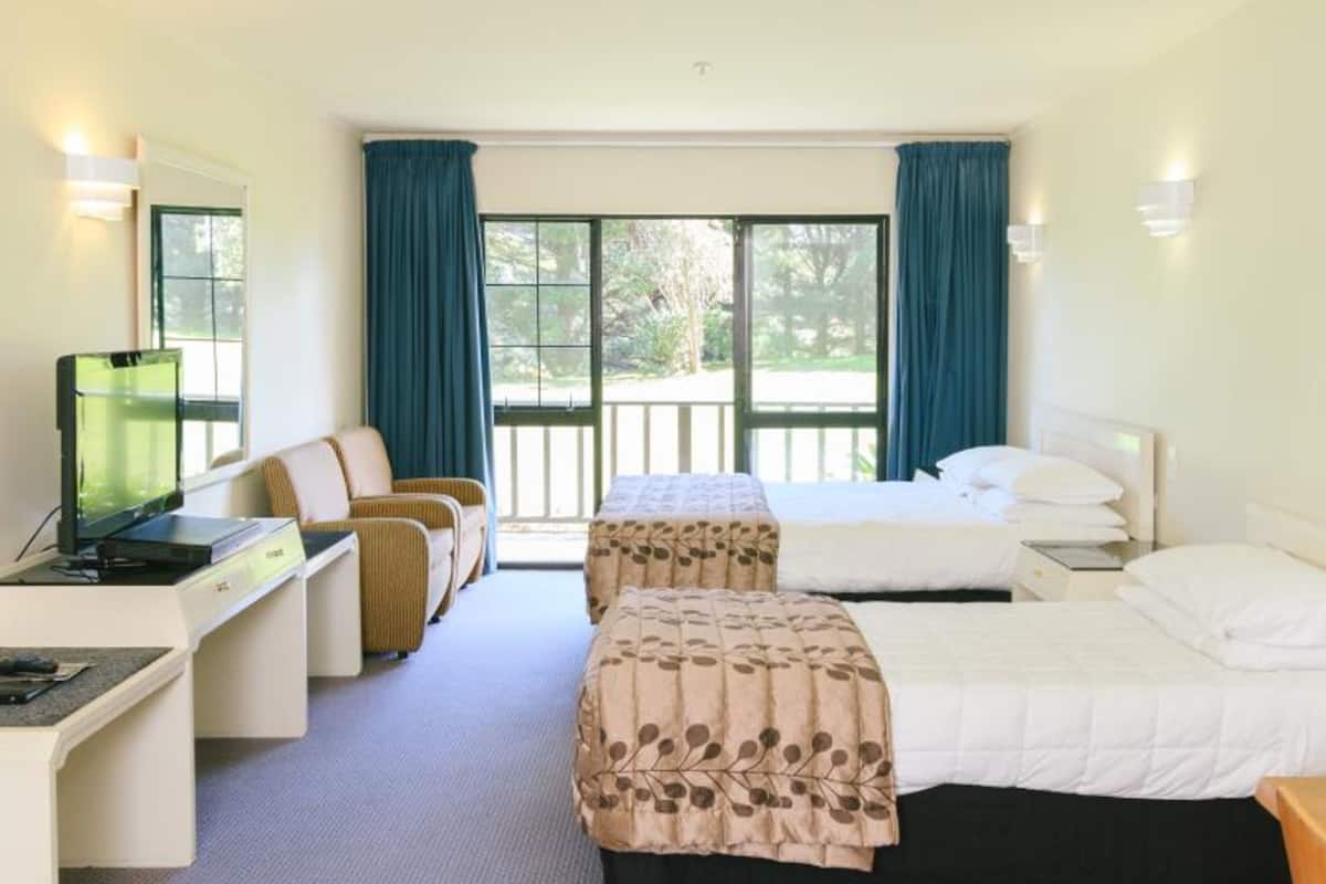 A hotel room with a desk, two beds, a TV, and large windows with curtains.