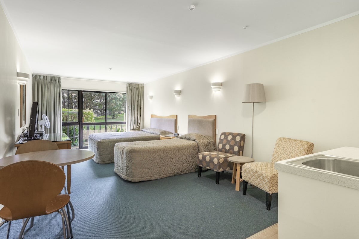 A hotel room with two beds, a dining table, a chair, a small table, a lamp, and a sink.