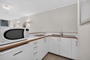 A compact kitchen with a microwave, wooden countertop, white cabinets, and a sink. - Capital Lodge Motor Inn (Wellington)