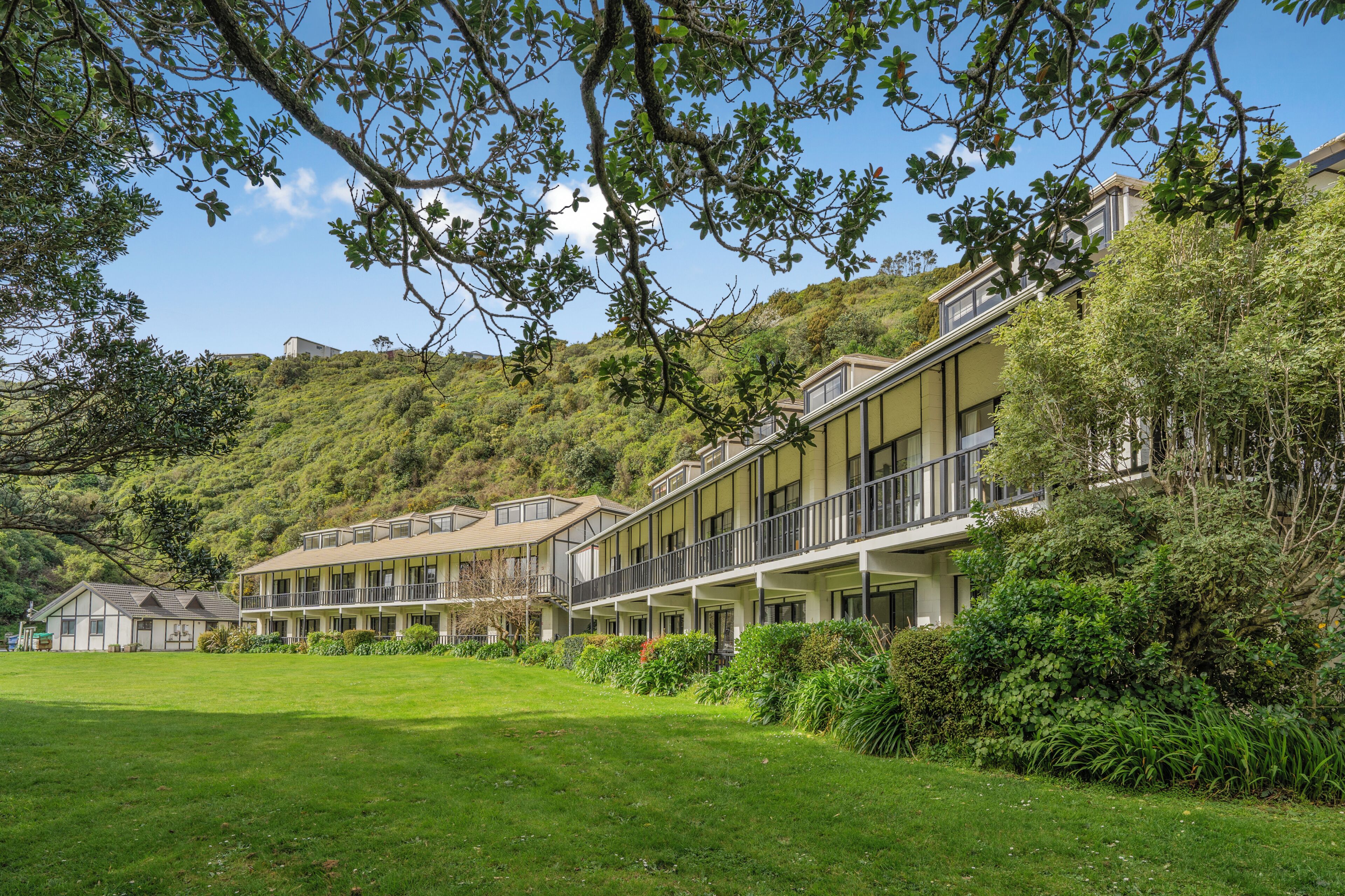 Un hotel con edificios de varios pisos, un césped cuidado y un paisaje montañoso de fondo.
