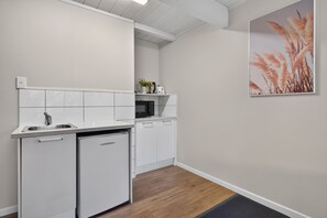 A compact kitchen with white cabinetry, a built-in microwave, and a small refrigerator. - Capital Lodge Motor Inn (Wellington)