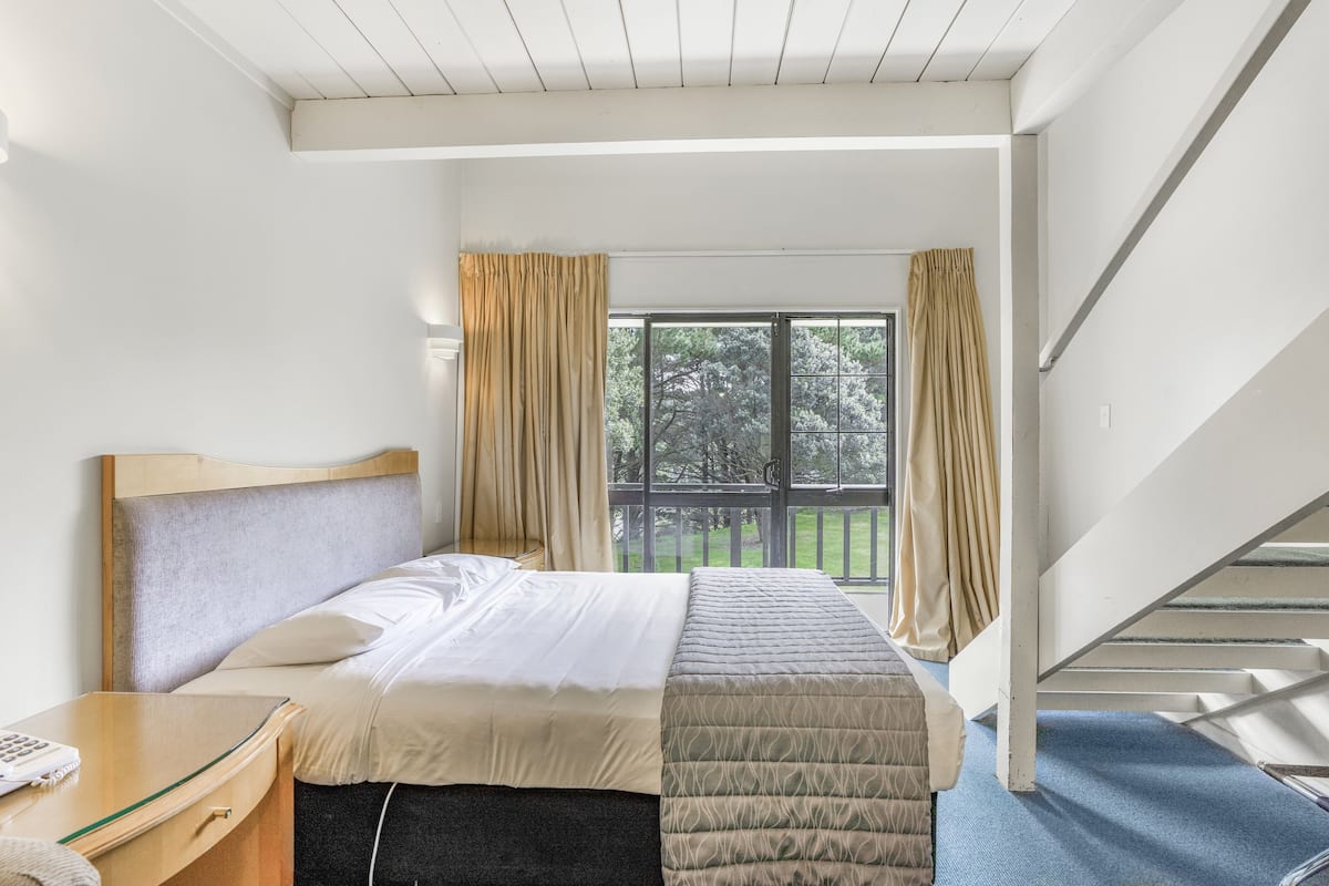 A hotel room with a bed, bedside table, and a window with curtains.
