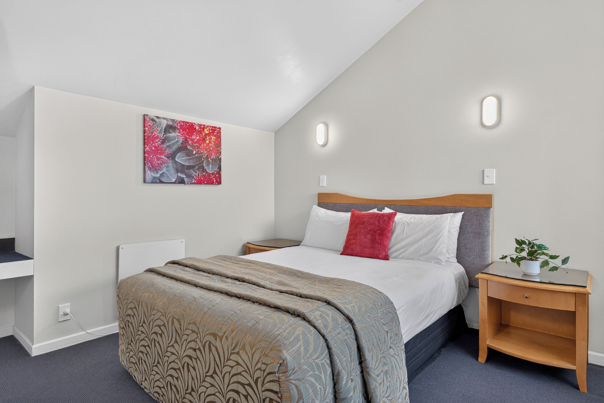 Quarto com cama, mesas de cabeceira, luminária na parede e um quadro.