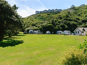 A campsite with RVs and caravans parked on a grassy field, surrounded by trees and hills.