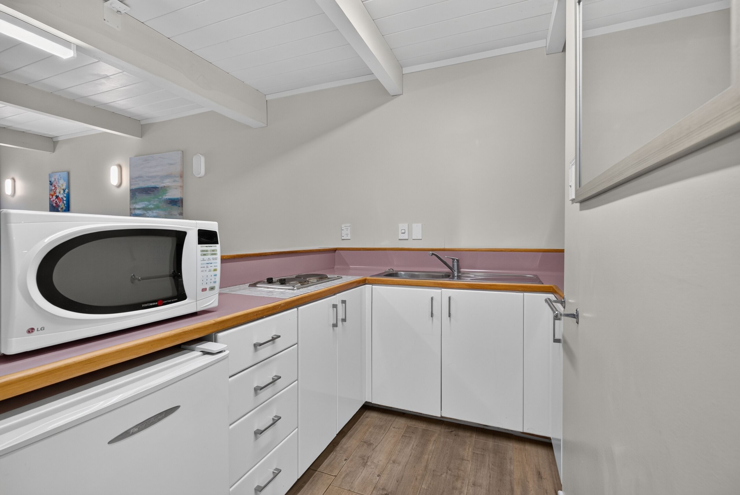 Cocina compacta con alacenas blancas, microondas, lavamanos y encimera de madera.
