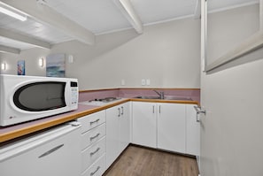 Cocina compacta con alacenas blancas, microondas, lavamanos y encimera de madera.