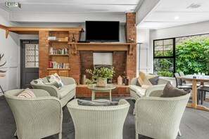 A cozy lounge area with wicker furniture, a fireplace, and a bookshelf. - Capital Lodge Motor Inn (Wellington)