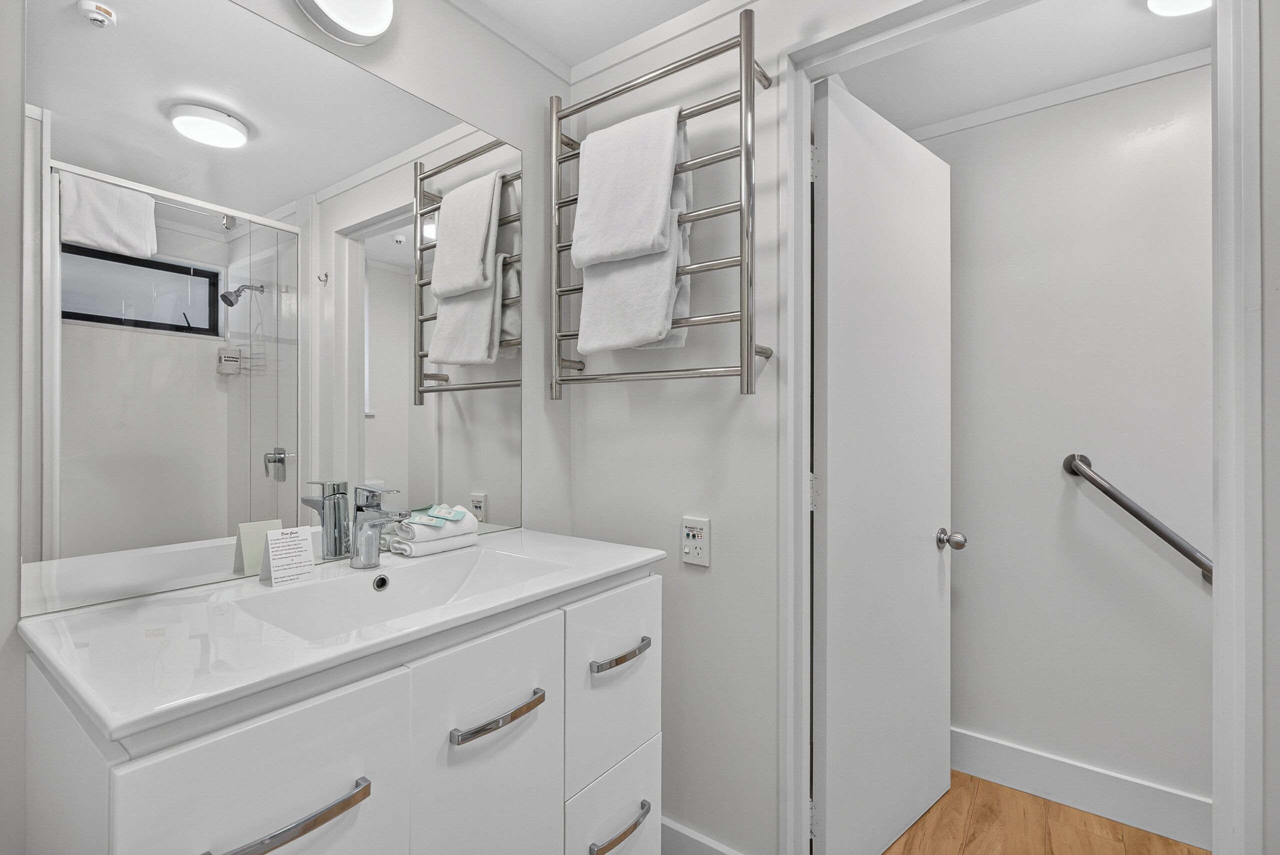 Une salle de bain moderne avec un meuble-lavabo blanc, un miroir, un porte-serviettes et un espace douche.