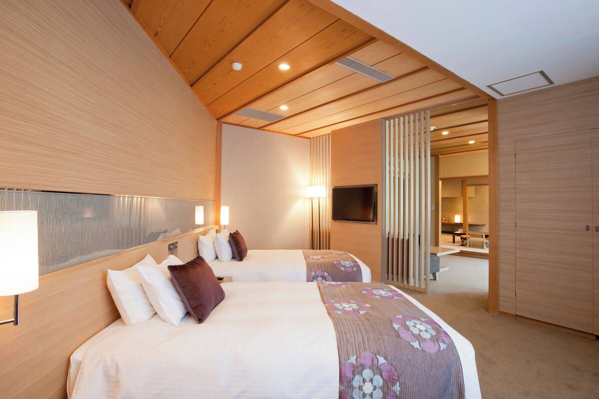 A hotel room with two beds, wooden ceiling, and a TV on the wall.