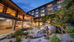 A modern hotel with a courtyard featuring a koi pond, rocks, and trees. - Miyajima Grand Hotel Arimoto (Hatsukaichi)